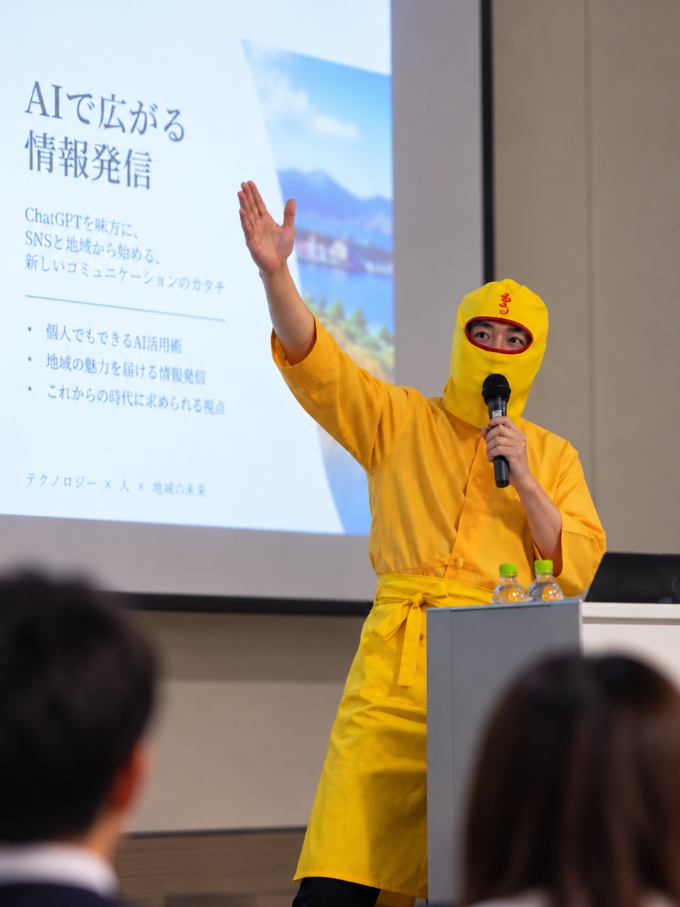黄色い衣装でマイクを持ち、AIについて講演するルウ王子